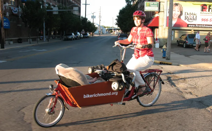Mom riding bakfiets cargo bike with baby and stroller