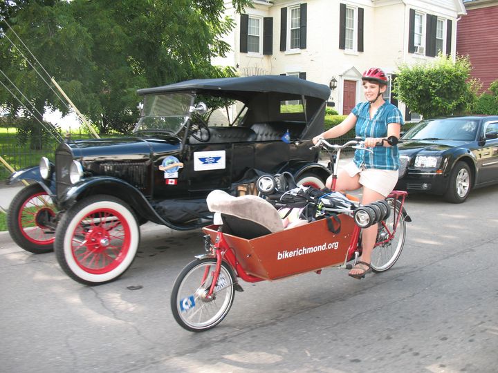 Bakfiets with car seat and stroller rides by a Model T car.