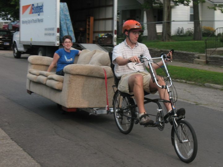 woman rides on full size coach being towed behind a recumbent bicycle