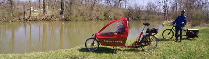 A bakfiets with a child in and a man with an longtail cargo bike take a break by a stream. 