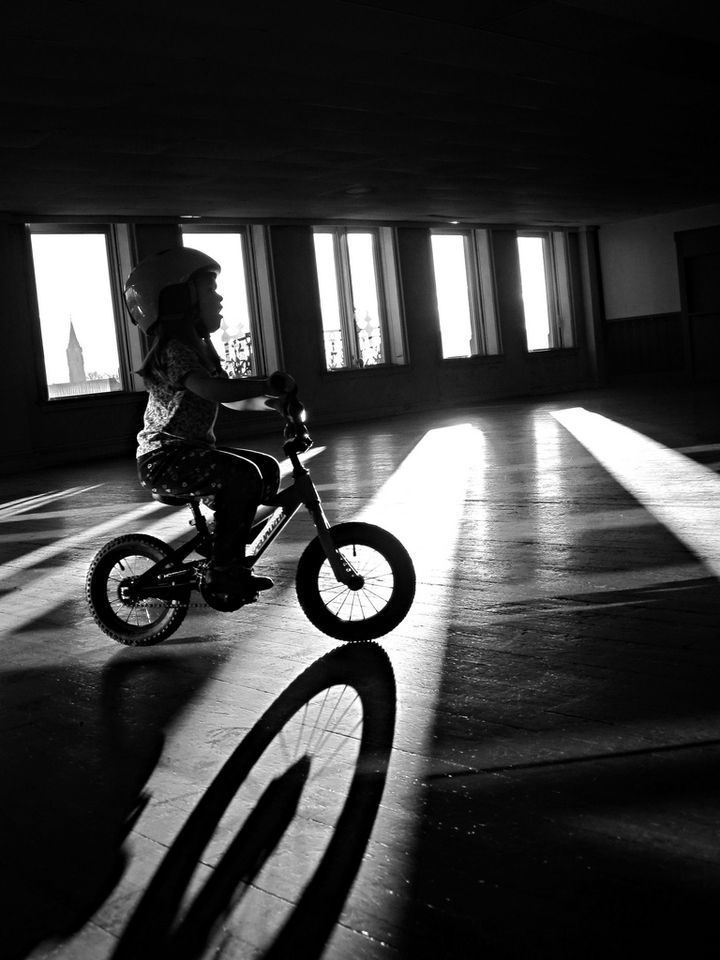 Back and white silhouette of child riding a push bike. 