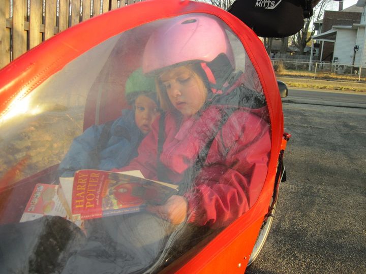  A big sister reads to her little brother under a bakfiets cargo bike weather canopy. 