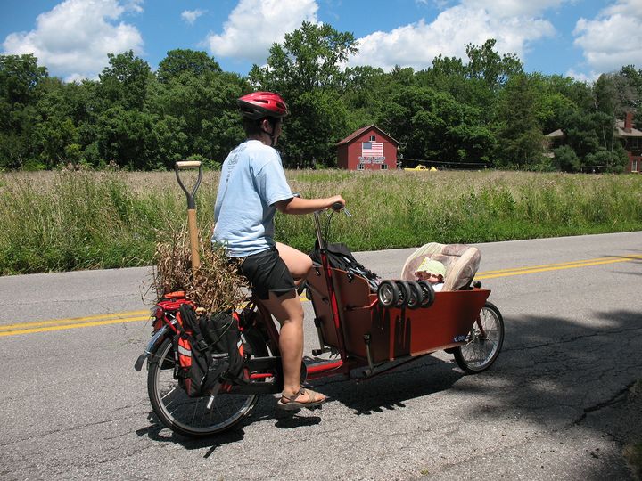 Mom rides with baby in bakfiets next to field and barn in Indiana
